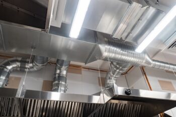 Ventilation Pipes In Silver Insulation Material. Chromed Pipes Hanging From Ceiling Inside Premises. Concept Is A Restaurant Exhaust System. Several Hoods In Room, Bottom View. Ventilation System